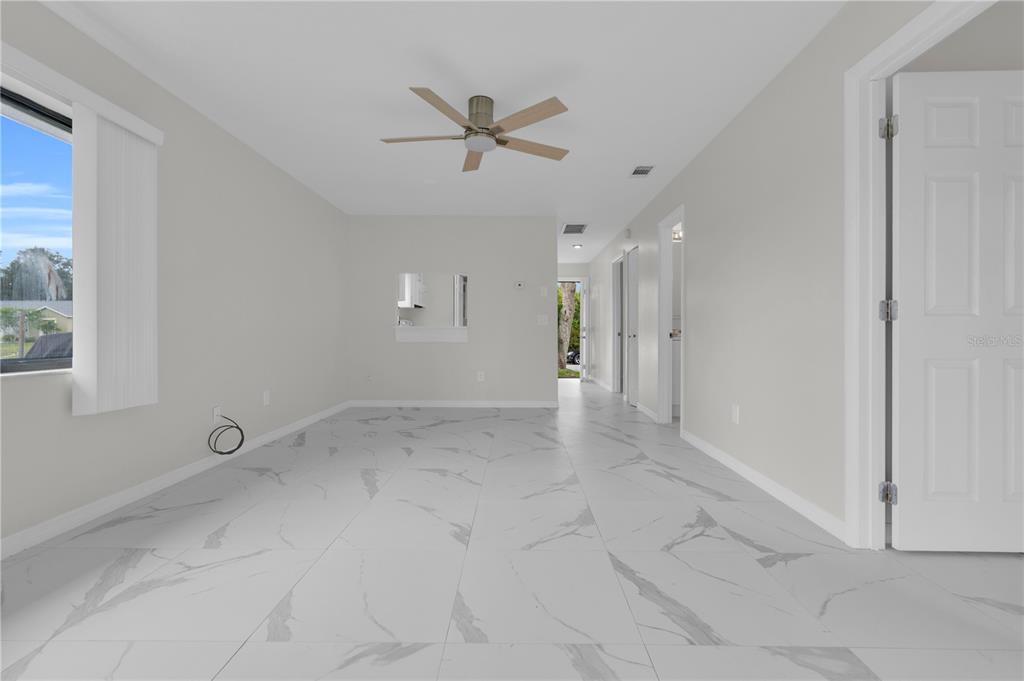 A bright, empty room features white marble-look tile flooring, a ceiling fan, and white walls — 6359 HERA STREET UNIT B, ENGLEWOOD, FL