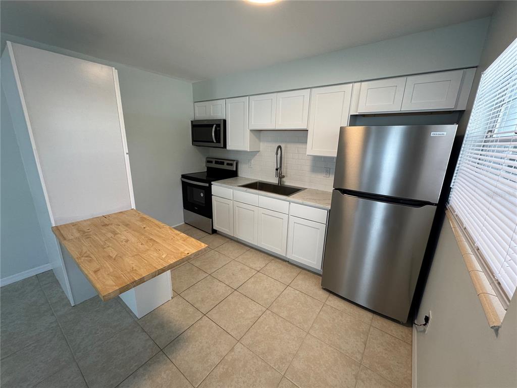 A kitchen features white cabinets, stainless steel appliances, a tile floor, and a wooden breakfast bar — 215 PARK BOULEVARD S UNIT A, VENICE, FL