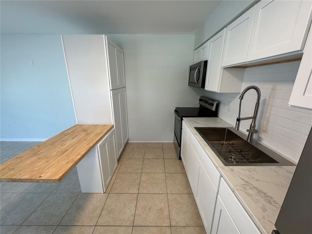 A kitchen features white cabinetry, a wood-topped breakfast bar, and stainless steel appliances — 215 PARK BOULEVARD S UNIT A, VENICE, FL