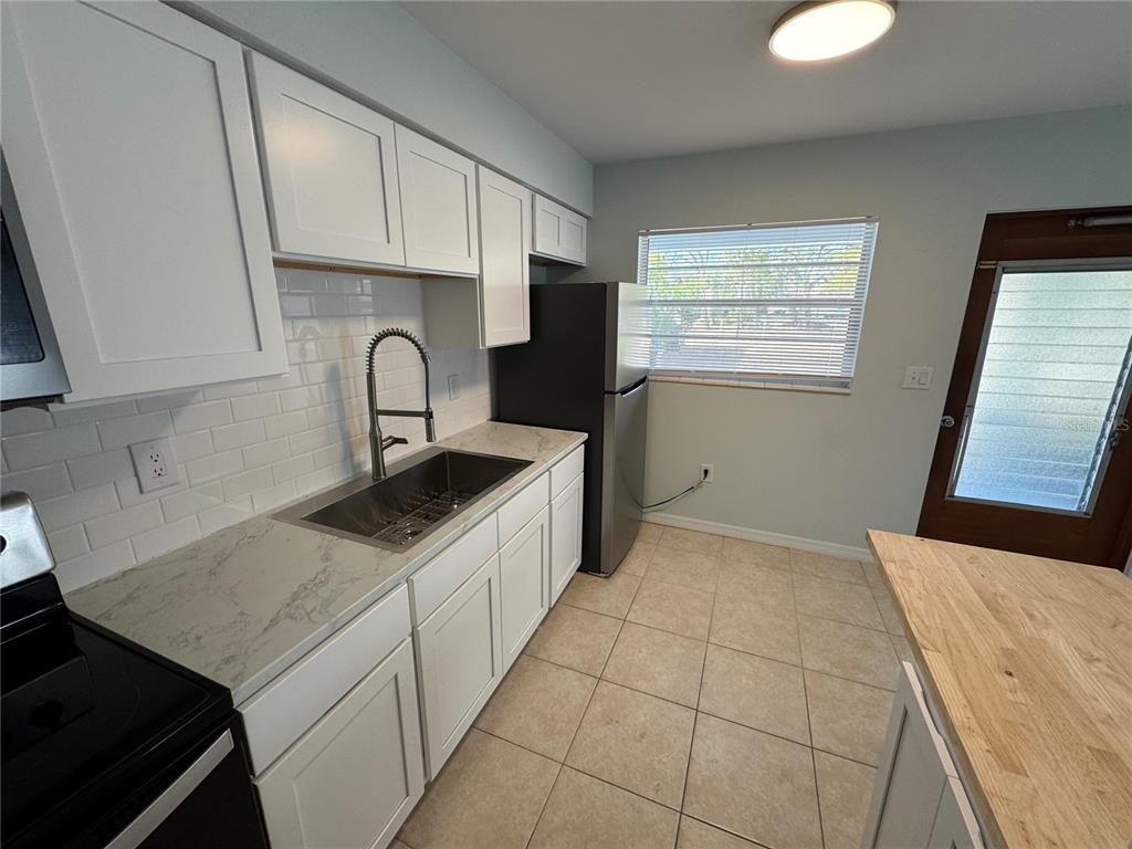 A kitchen features white cabinets, a stainless steel sink, a refrigerator, and light-colored tile flooring — 215 PARK BOULEVARD S UNIT A, VENICE, FL