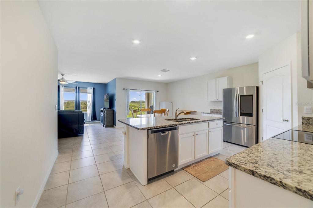 A kitchen with white cabinets, granite countertops, and stainless steel appliances overlooks an open living area — 2135 E OLD MILL DRIVE, DELTONA, FL