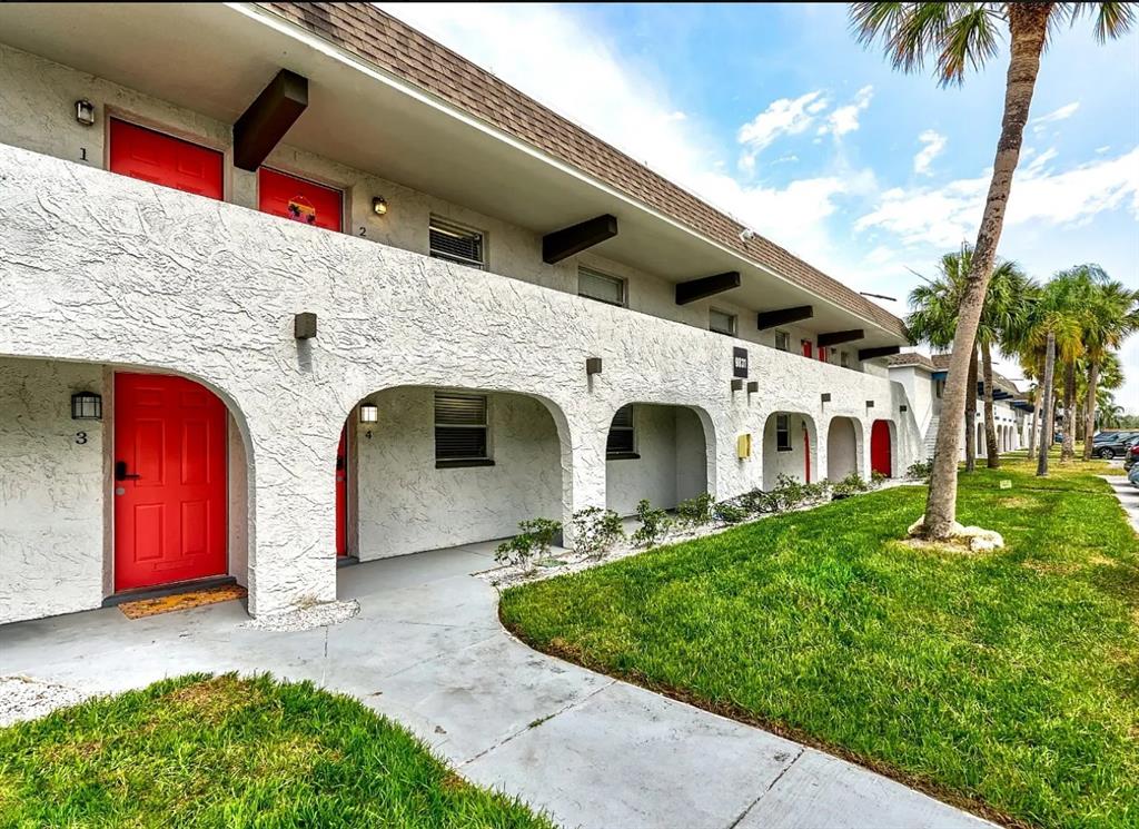 A two-story apartment building exterior features white stucco walls, arched walkways, and red doors — 9911 AQUARIUS DRIVE UNIT 8, PORT RICHEY, FL