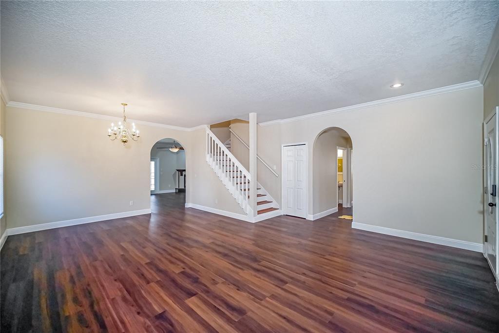 A spacious room with wood-look flooring, a white staircase, and arched doorways — 2509 SKIF DRIVE, ORLANDO, FL