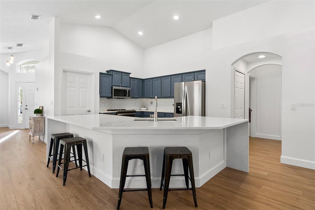 A kitchen features a white quartz island with bar stools, blue cabinets, and stainless appliances — 14018 BUDWORTH CIRCLE, ORLANDO, FL