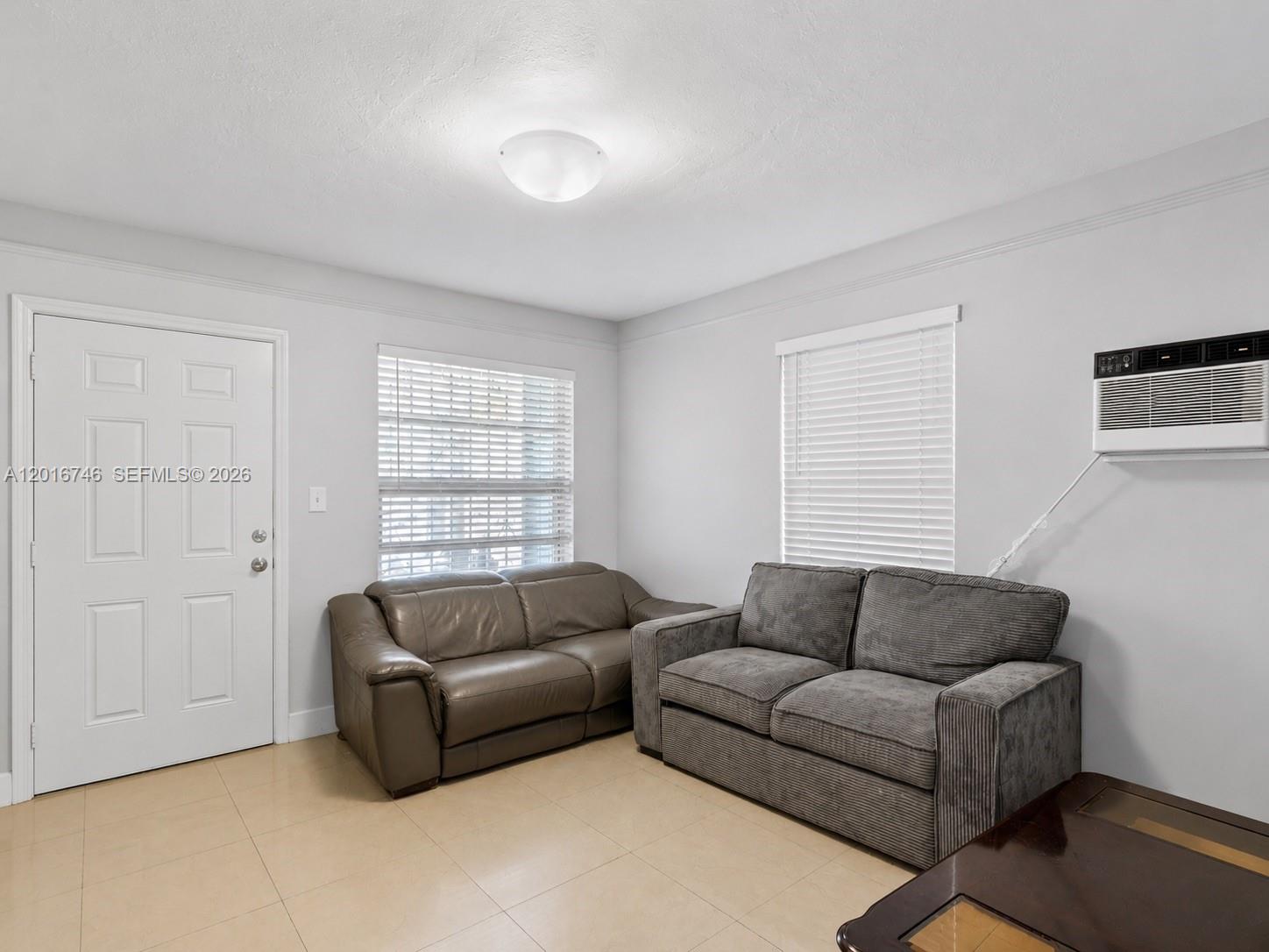 A living room features two sofas, tile flooring, two windows with blinds, and a wall-mounted AC — 1111 NW 77th St, Miami FL 33150, MIAMI, FL