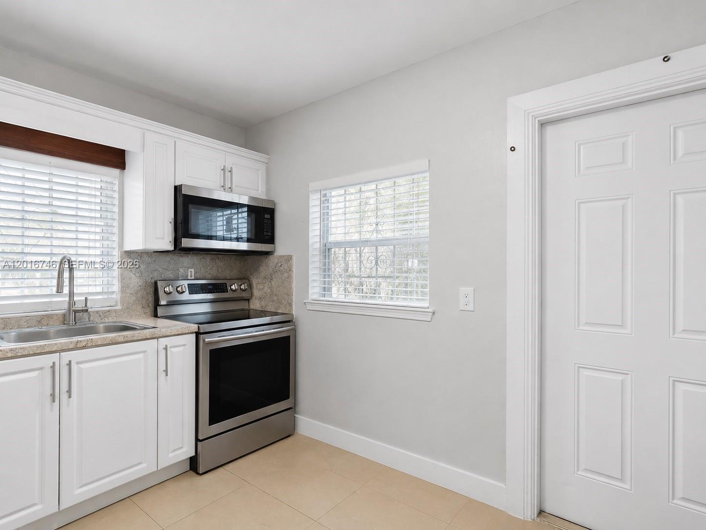 A kitchen features white cabinets, stainless steel appliances, a window, and light-colored tile flooring — 1111 NW 77th St, Miami FL 33150, MIAMI, FL