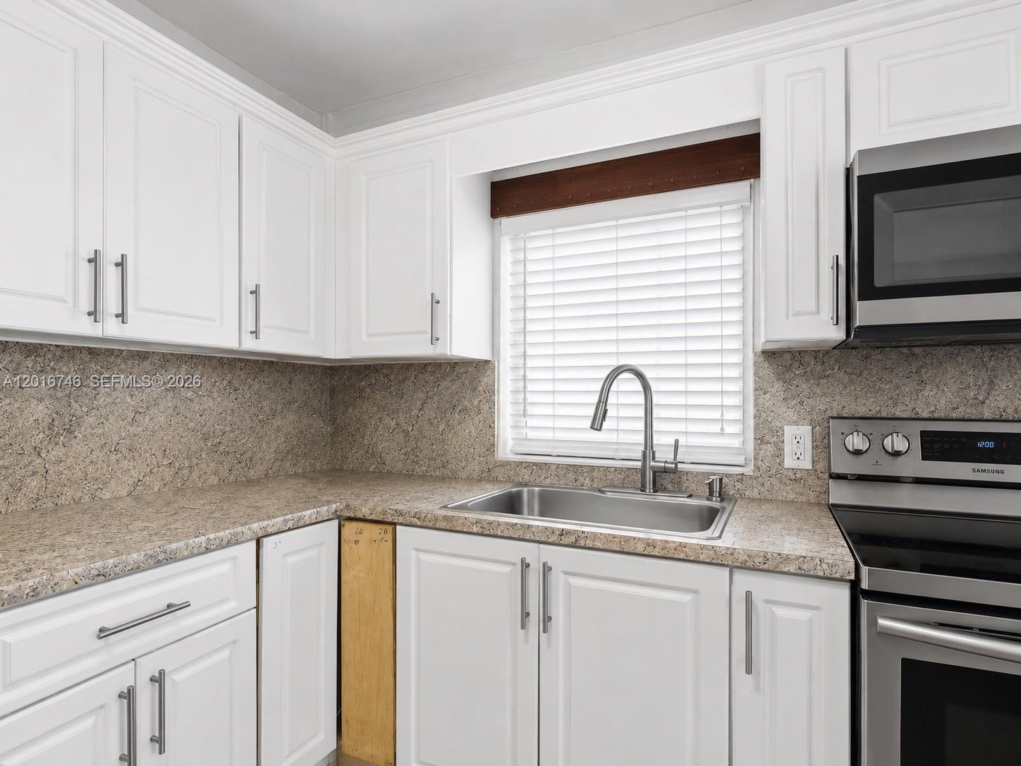 A kitchen features white cabinets, a stainless steel sink, and speckled laminate countertops — 1111 NW 77th St, Miami FL 33150, MIAMI, FL