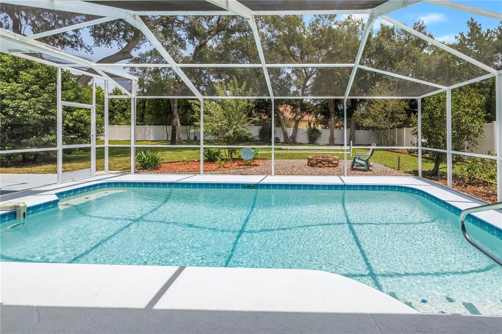 A swimming pool with a screened enclosure overlooks a backyard with a fire pit — 18812 BASCOMB LANE, HUDSON, FL