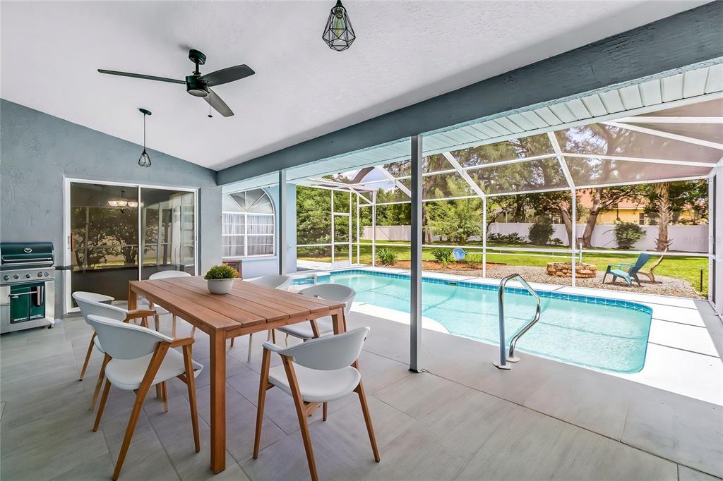 A covered patio features a dining table, a grill, and a screened-in swimming pool — 18812 BASCOMB LANE, HUDSON, FL