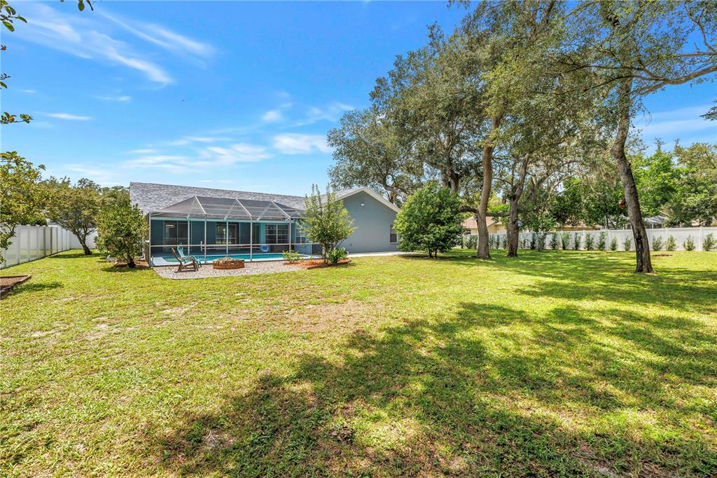 A backyard features a screened-in pool, a fire pit, and large trees on a lawn — 18812 BASCOMB LANE, HUDSON, FL