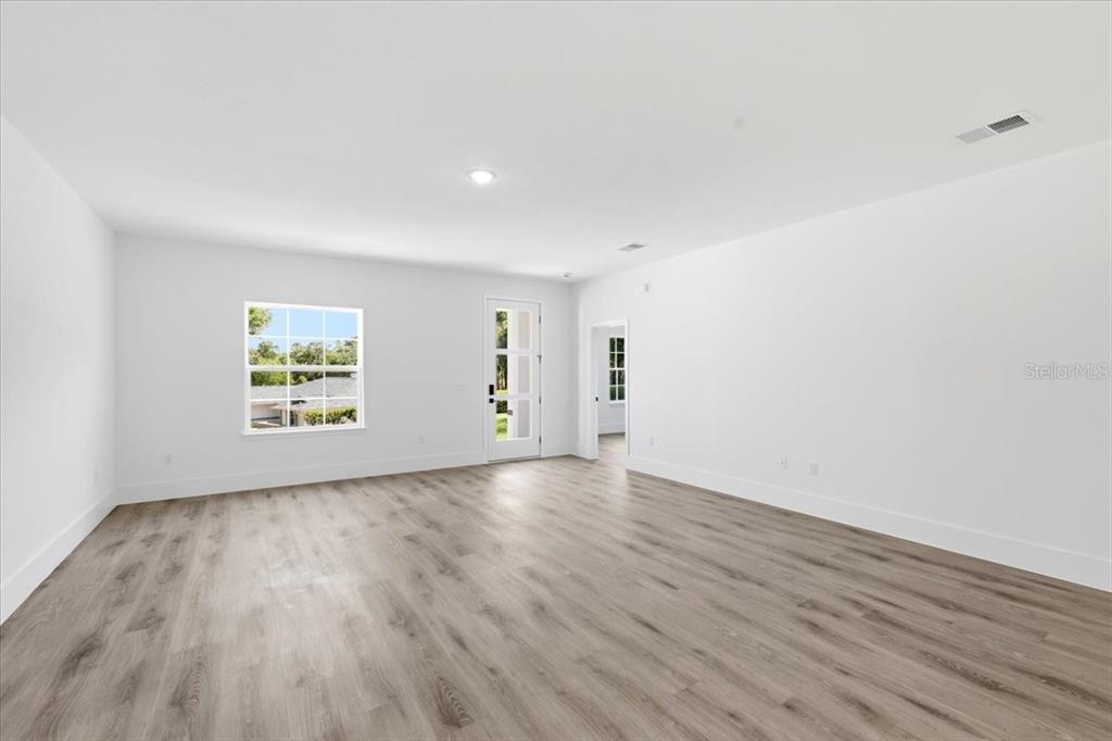 An empty room features white walls, light wood-look flooring, a window, and a glass-paneled door — 2670 W FAIRWAY LOOP, CITRUS SPRINGS, FL