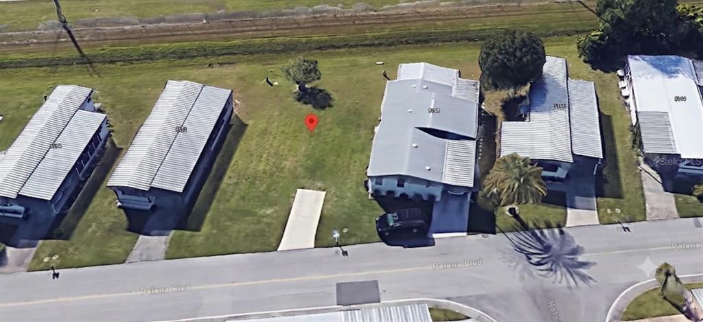 An aerial view shows a vacant grassy lot situated between two mobile homes on a street — 5150 PALENA BOULEVARD UNIT 294, NORTH PORT, FL