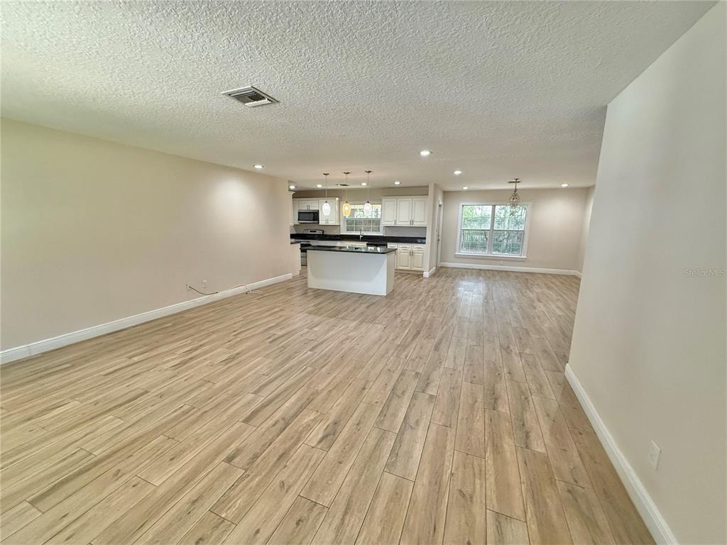 An open-concept living area features light wood-look flooring and a kitchen with white cabinetry — 2810 FLOWERTREE ROAD, BELLE ISLE, FL