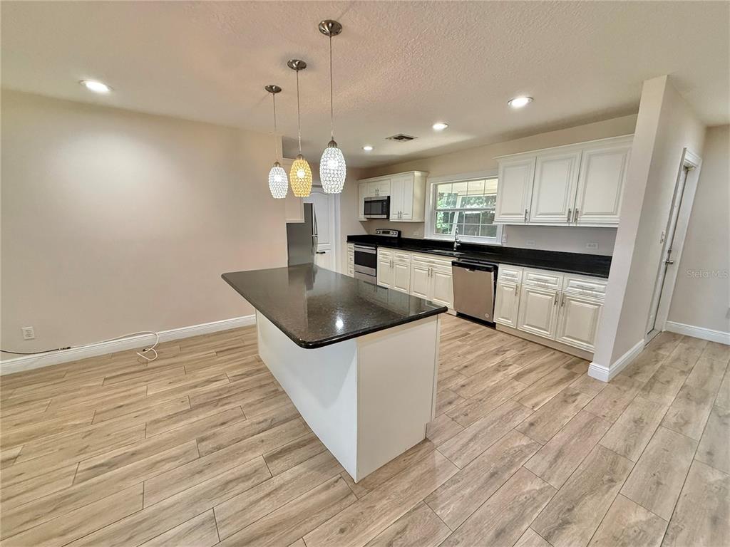 A kitchen features white cabinets, a dark countertop island, and wood-look flooring — 2810 FLOWERTREE ROAD, BELLE ISLE, FL