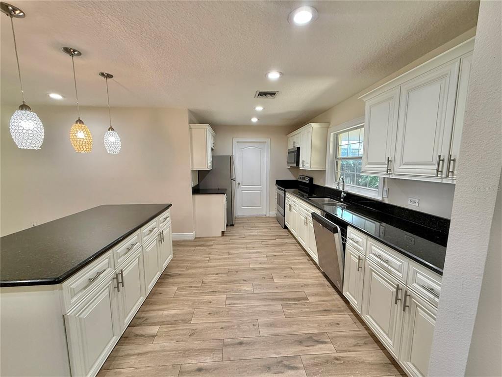 A kitchen features white cabinets, black countertops, stainless steel appliances, and wood-look tile flooring — 2810 FLOWERTREE ROAD, BELLE ISLE, FL