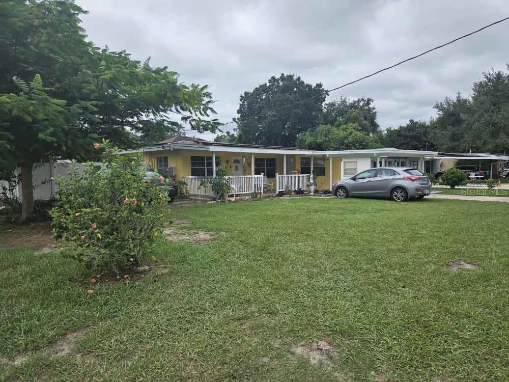 A yellow single-story house with a white front porch sits behind a large grassy yard — 3902 CASTELL DRIVE, ORLANDO, FL