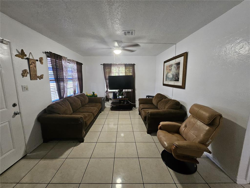 A living room features tile flooring, two brown sofas, a recliner, and a television stand — 3902 CASTELL DRIVE, ORLANDO, FL