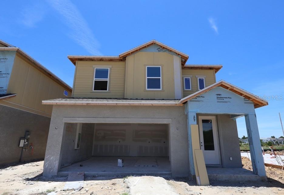 A two-story house exterior features a light green stucco finish, white trim, and an open garage — 3435 YELLOW CASSIA DRIVE, WESLEY CHAPEL, FL