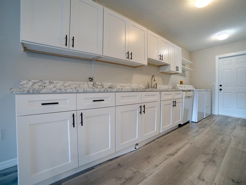 A laundry room features white shaker cabinets, marble-look countertops, and light wood-look flooring — 488 W ROSEWOOD LANE UNIT 488, TAVARES, FL