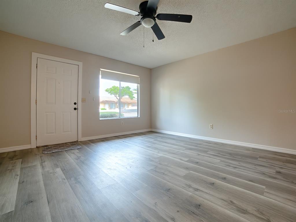 An empty living room features light gray wood-look flooring, beige walls, and a ceiling fan — 488 W ROSEWOOD LANE UNIT 488, TAVARES, FL