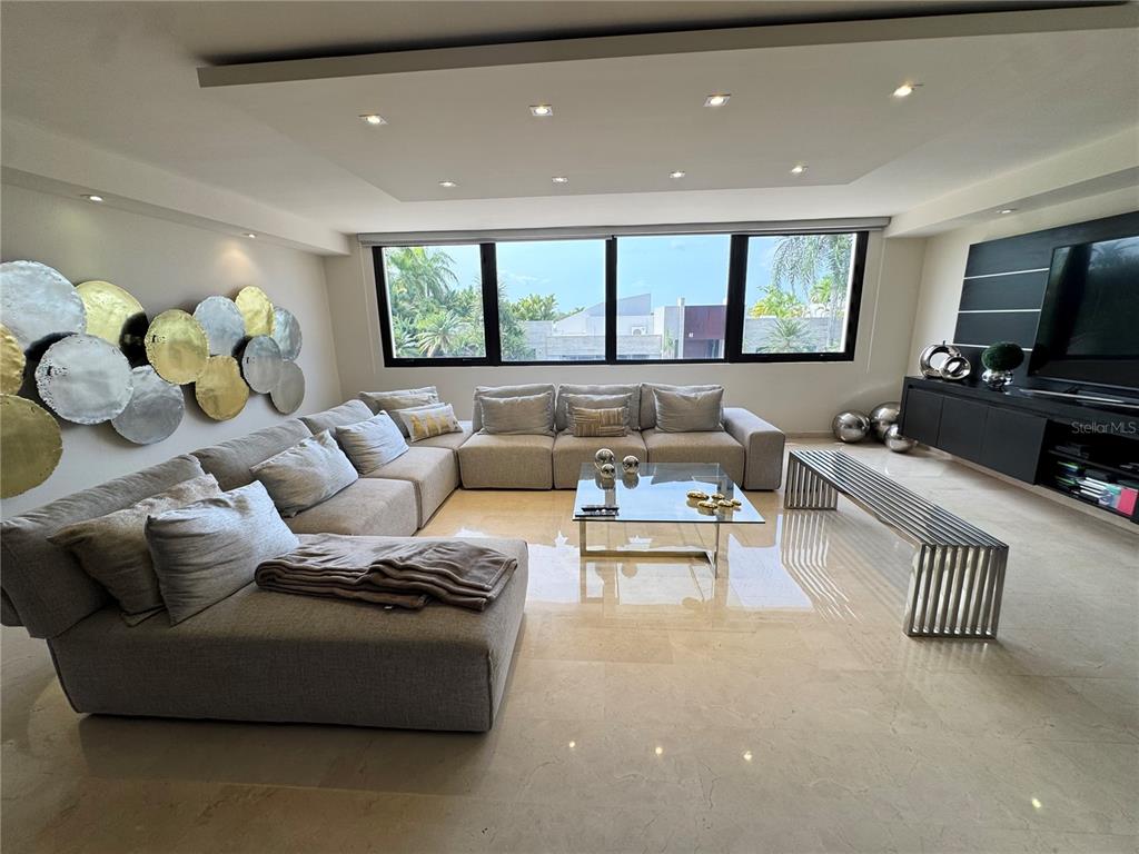 A modern living room features a large sectional sofa, a glass coffee table, and tile flooring — #9 Palma Real ESTANCIAS DE TORRIMAR, GUAYNABO, PR