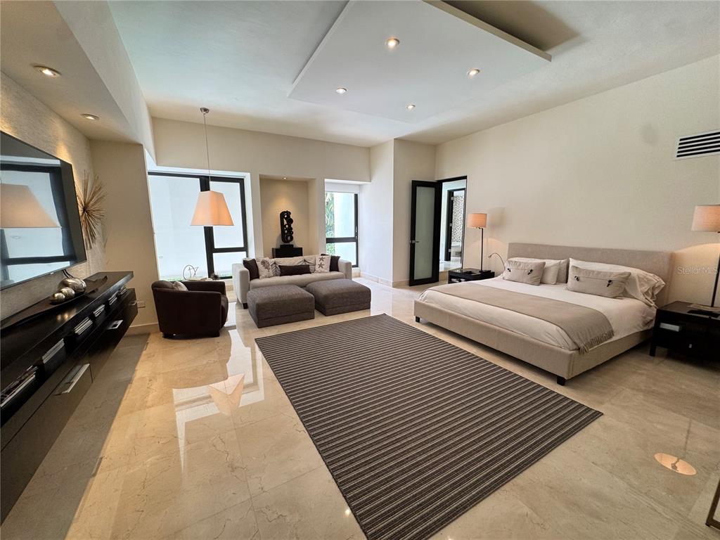 A spacious bedroom features a large bed, a seating area, and polished stone flooring — #9 Palma Real ESTANCIAS DE TORRIMAR, GUAYNABO, PR