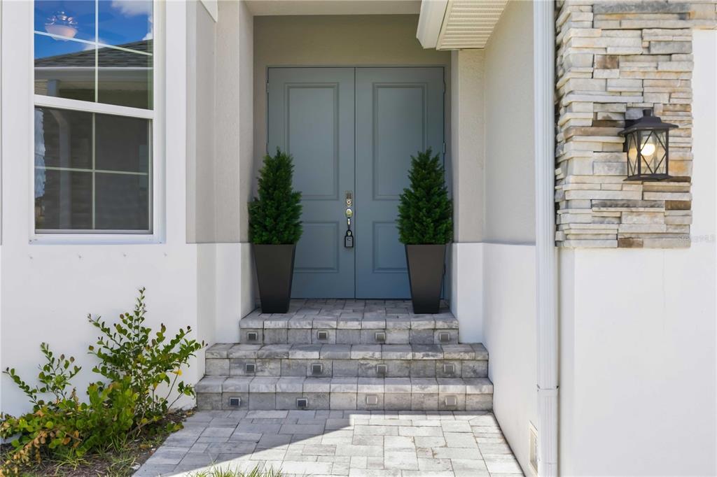 A front entrance features double blue doors, stone steps, and two potted evergreen trees — 2483 HERRON TERRACE, PORT CHARLOTTE, FL