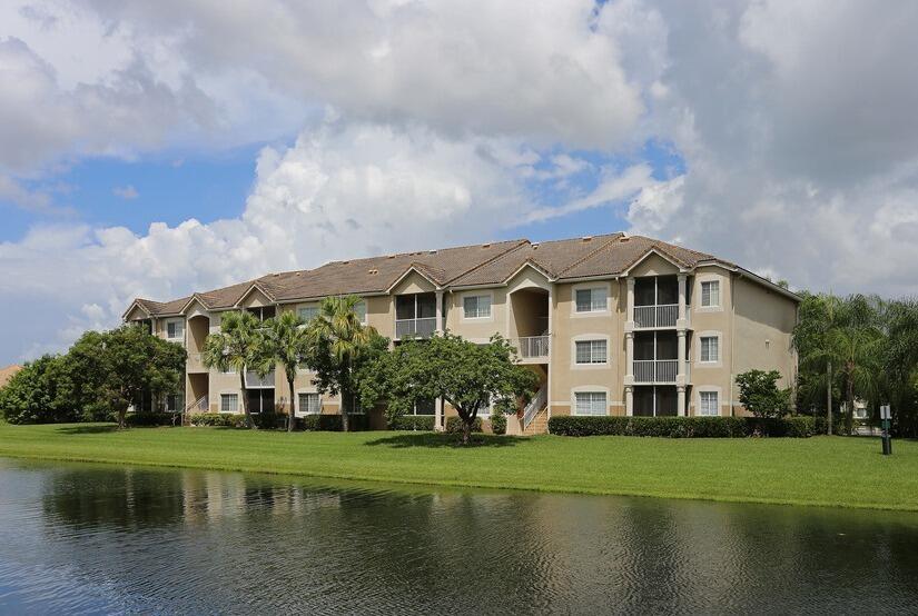 A three-story apartment building sits behind a grassy lawn and a calm pond — 8935 Okeechobee Boulevard # 204, West Palm Beach FL 33411, WEST PALM BEACH, FL