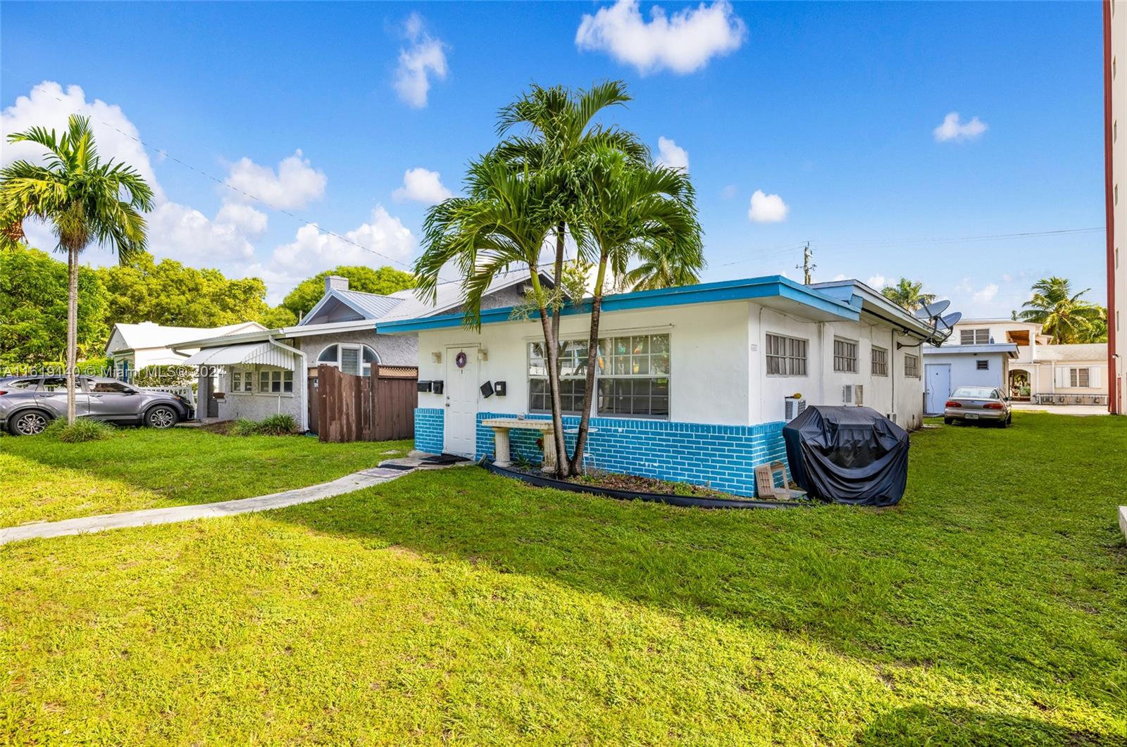 A single-story house with white walls and a blue brick base sits on a lawn — 1711 Buchanan St, Hollywood FL 33020, HOLLYWOOD, FL