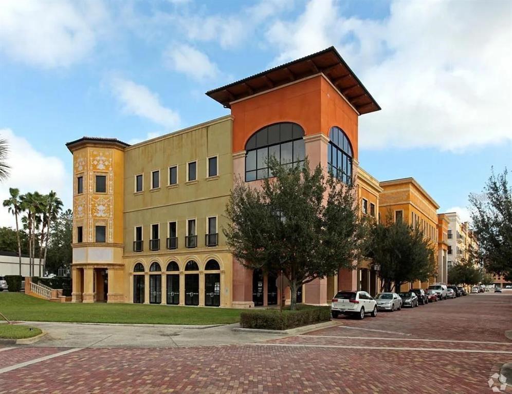 A multi-story commercial building with orange and yellow stucco walls sits beside a brick street — 7065 WESTPOINTE BOULEVARD UNIT 305, ORLANDO, FL