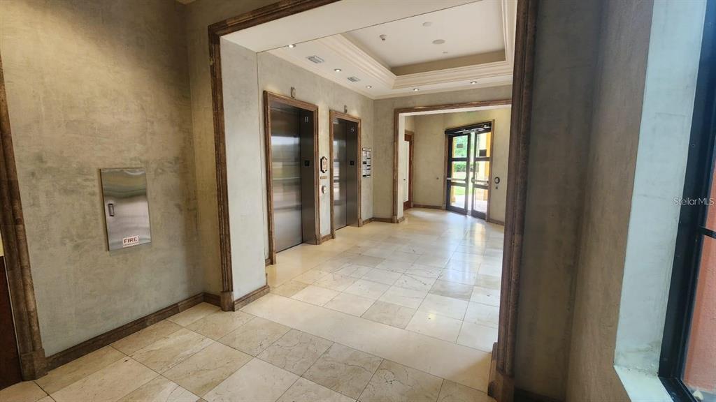 A lobby area features two stainless steel elevators, tiled floors, and glass-paned double doors — 7065 WESTPOINTE BOULEVARD UNIT 305, ORLANDO, FL