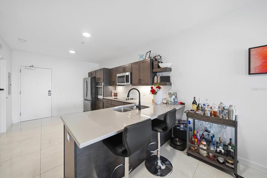 A modern kitchen features dark wood cabinetry, a quartz island with bar stools, and stainless appliances — 132 MIRROR LAKE UNIT 403, ST PETERSBURG, FL