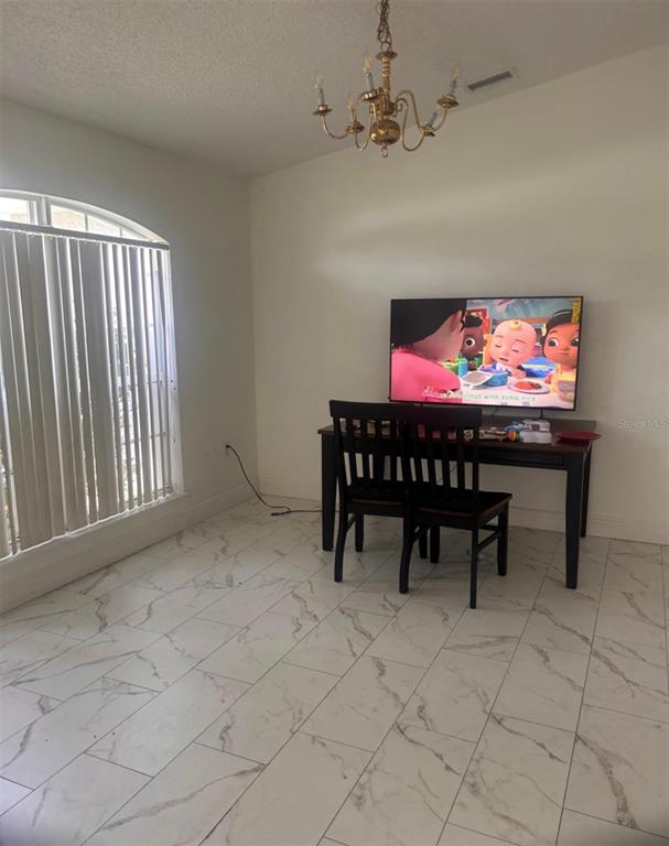 A dining area features white marble-look tile flooring, a dark wooden table, and a chandelier — 33 COVENTRY COURT, KISSIMMEE, FL