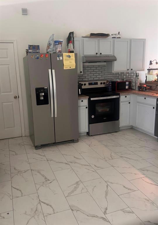A kitchen features stainless steel appliances, white cabinets, a gray tiled backsplash, and marble-look flooring — 33 COVENTRY COURT, KISSIMMEE, FL