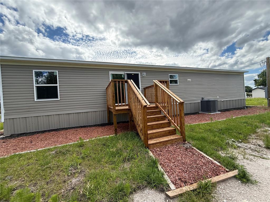The exterior of a manufactured home features light gray siding, a wooden staircase, and red mulch — 4246 LA SALLE AVENUE, ST CLOUD, FL