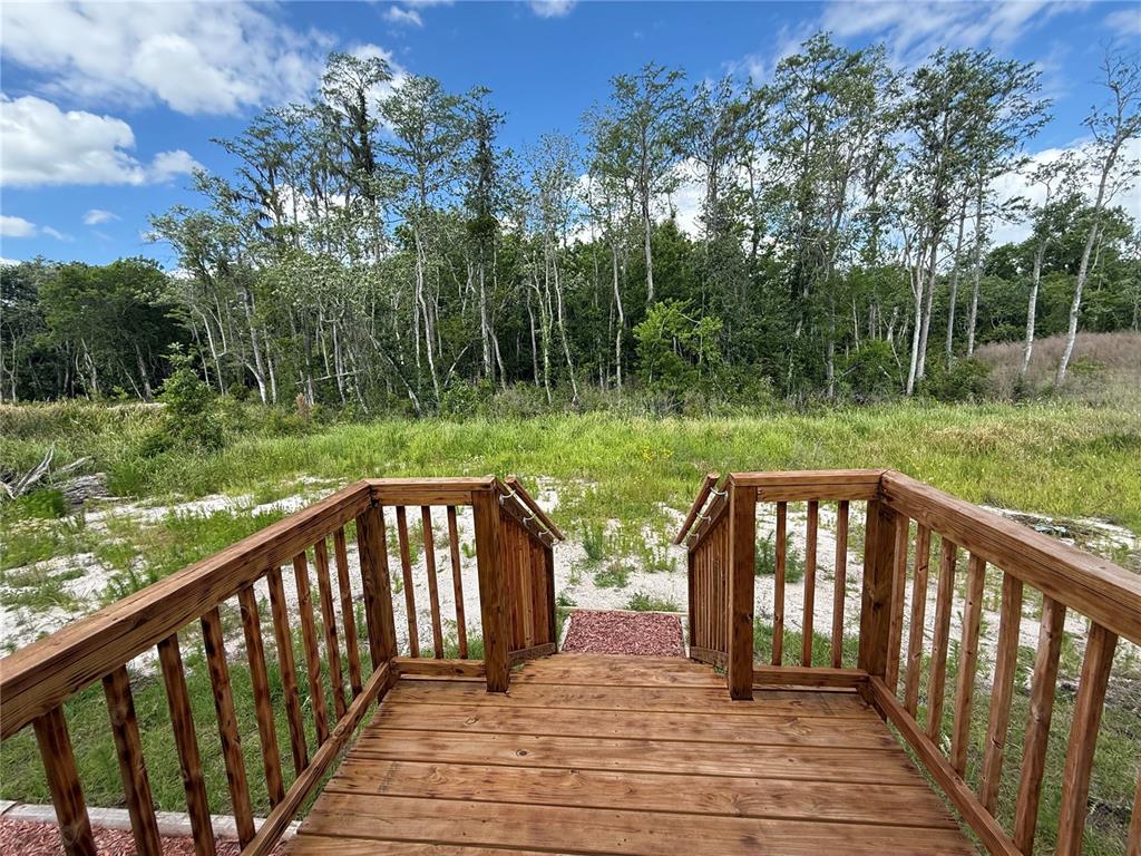 A wooden deck with railings overlooks a grassy field and a line of trees — 4246 LA SALLE AVENUE, ST CLOUD, FL