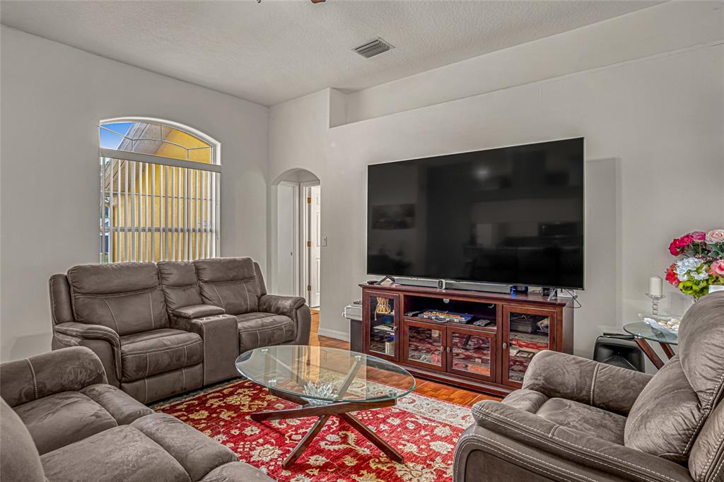 A living room features brown leather furniture, a red patterned rug, and a large television — 525 JUSTINE AVENUE NW, PALM BAY, FL