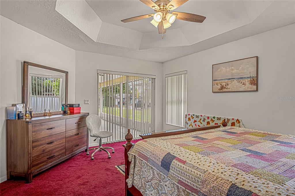 A bedroom with a tray ceiling, red carpet, wooden dresser, and sliding glass doors — 525 JUSTINE AVENUE NW, PALM BAY, FL