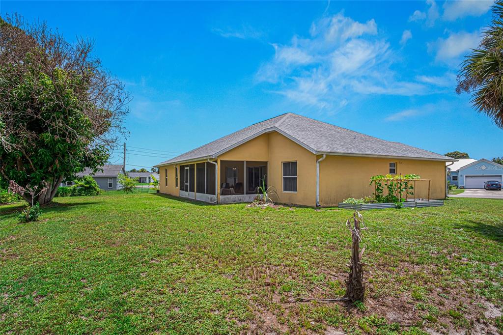 The rear exterior of a yellow house features a screened-in porch and a garden bed — 525 JUSTINE AVENUE NW, PALM BAY, FL