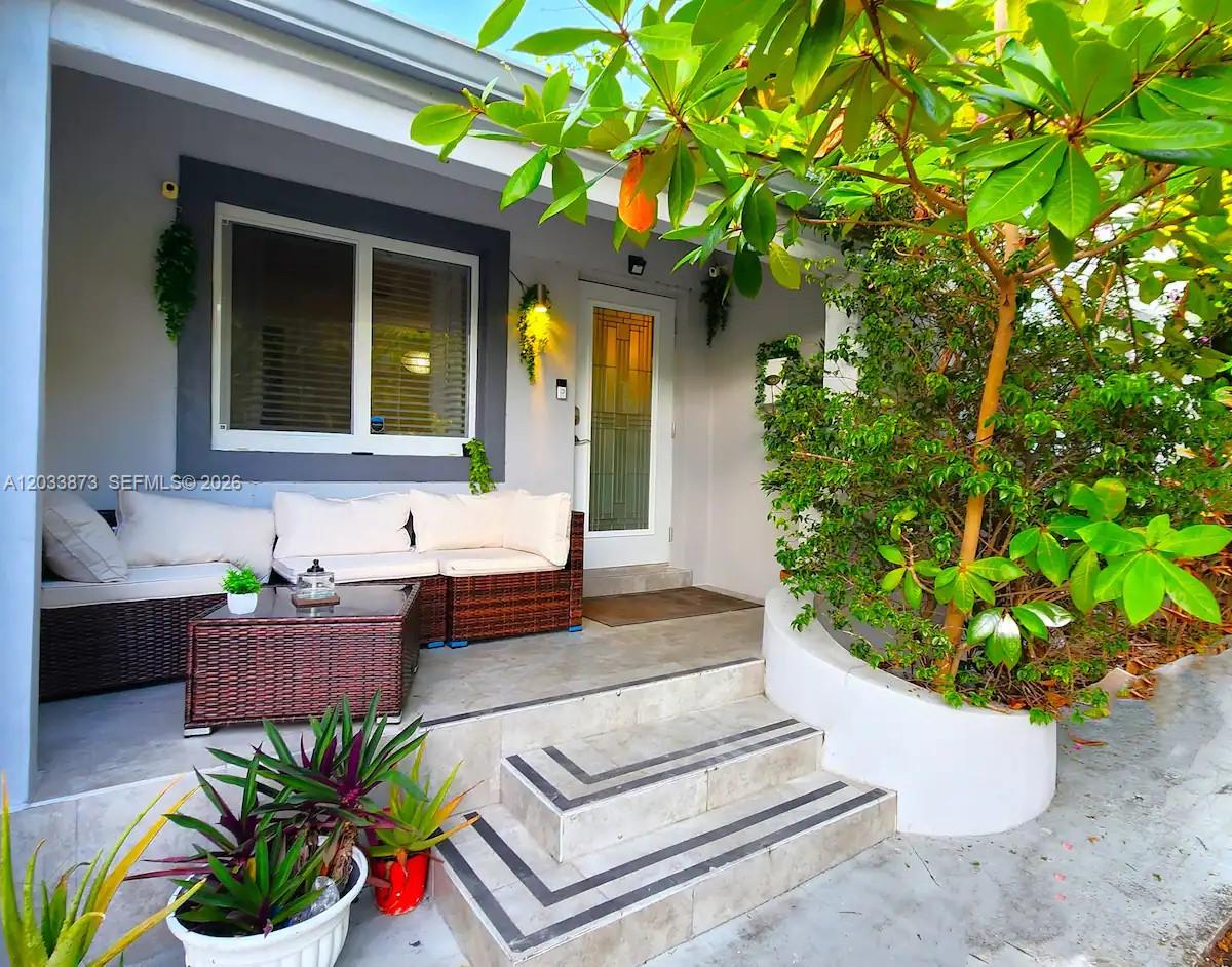A covered patio features wicker furniture, a coffee table, and steps leading to a front door — 11 NW 47th Ter, Miami FL 33127, MIAMI, FL