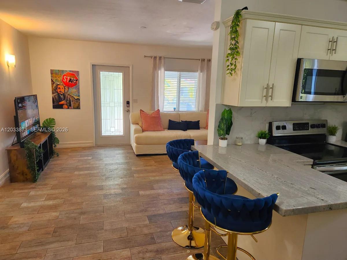 A kitchen with a breakfast bar and stools opens into a living area with tile floors — 11 NW 47th Ter, Miami FL 33127, MIAMI, FL