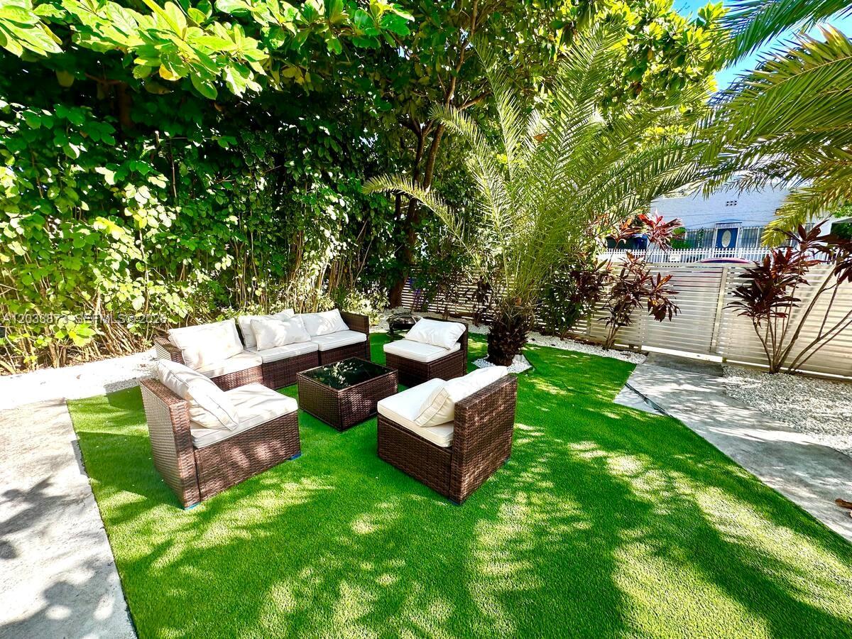 A backyard patio features artificial turf, wicker lounge furniture, and lush tropical landscaping — 11 NW 47th Ter, Miami FL 33127, MIAMI, FL