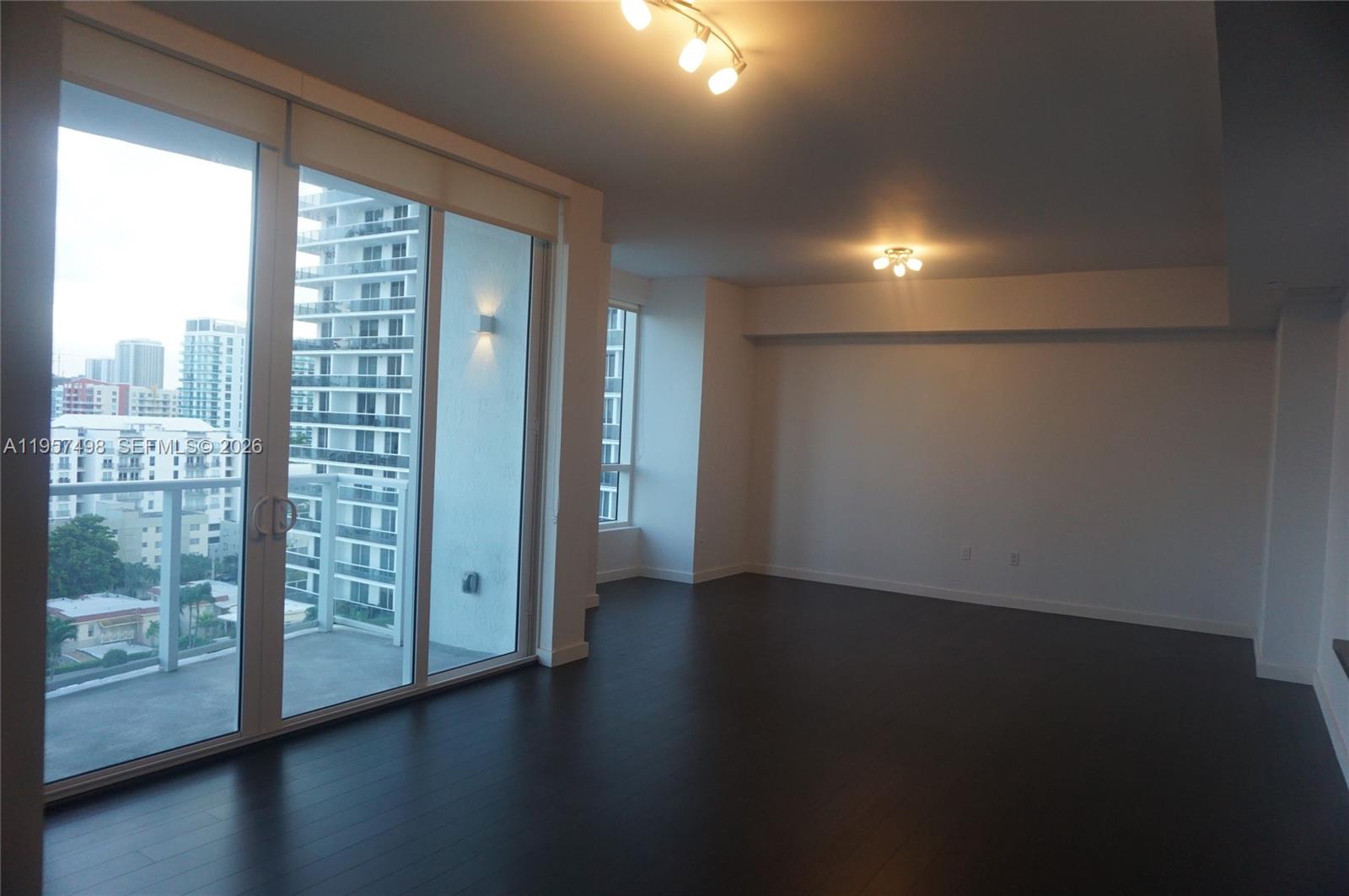 An empty living room features dark hardwood floors, white walls, and a sliding glass balcony door — 601 NE 27TH ST # 1706, Miami FL 33137, MIAMI, FL