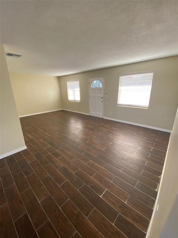 An empty living room features light-colored walls, a white front door, and dark wood-look flooring — 803 HASELTON STREET, EUSTIS, FL