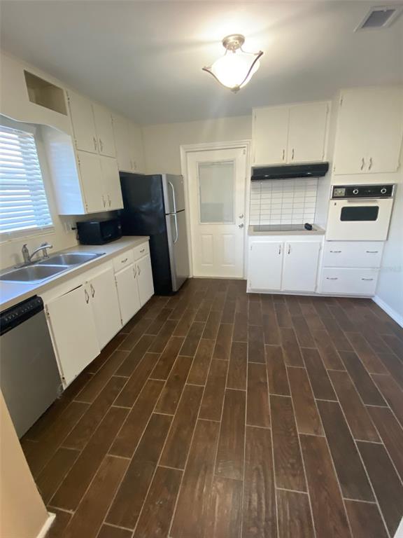 A kitchen features white cabinets, dark wood-look tile flooring, a black refrigerator, and built-in appliances — 803 HASELTON STREET, EUSTIS, FL