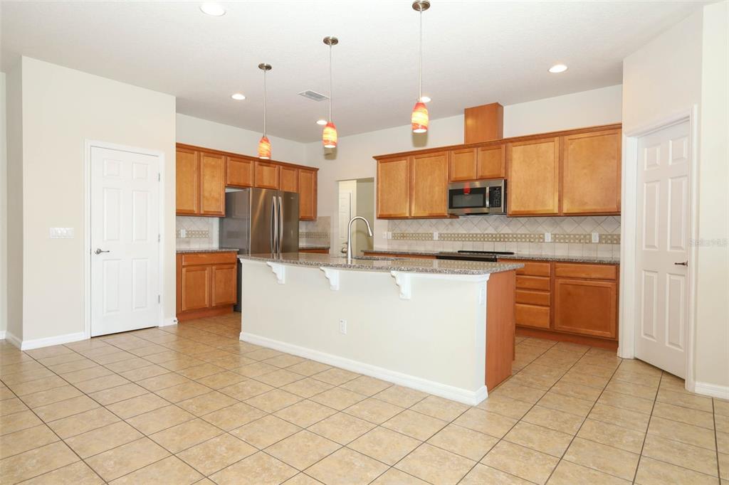 A kitchen with wood cabinets, granite countertops, stainless steel appliances, and tile flooring — 2610 MEAD AVENUE, ST CLOUD, FL
