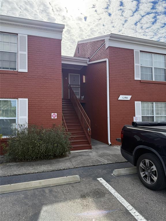 A two-story red brick apartment building features an exterior staircase leading to an upper entrance — 1290 83RD AVENUE N UNIT D, ST PETERSBURG, FL