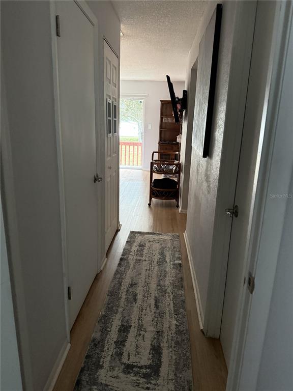 A hallway with light wood flooring leads to a doorway with a view of outdoors — 1290 83RD AVENUE N UNIT D, ST PETERSBURG, FL