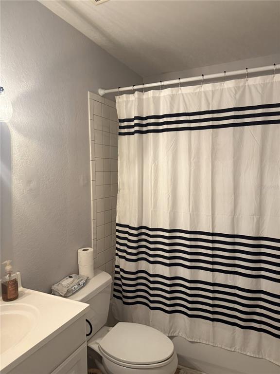A bathroom features a white vanity, a toilet, and a shower with a striped curtain — 1290 83RD AVENUE N UNIT D, ST PETERSBURG, FL