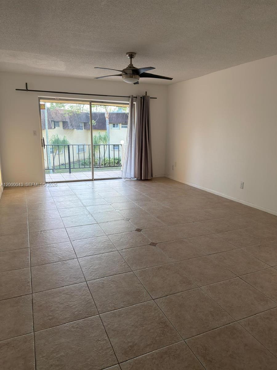 An empty room features beige tile flooring, a ceiling fan, and a sliding glass door — 9108 SW 137th Ter # 3, Miami FL 33176, MIAMI, FL
